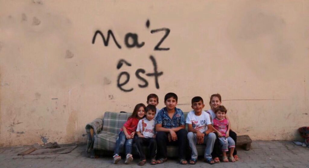 Children sitting under Ma'z Êst writing on a wall